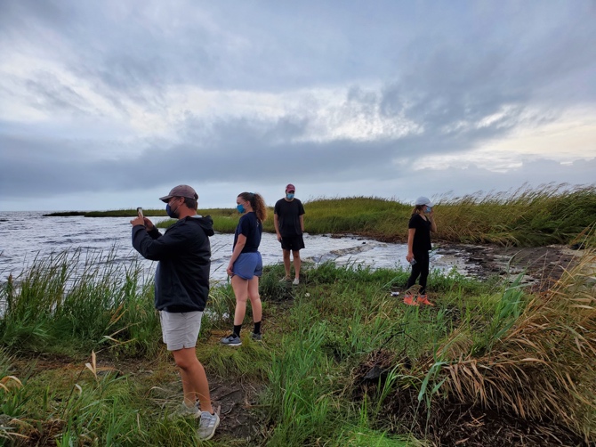 A group of people standing in grass near water AI-generated content may be incorrect.